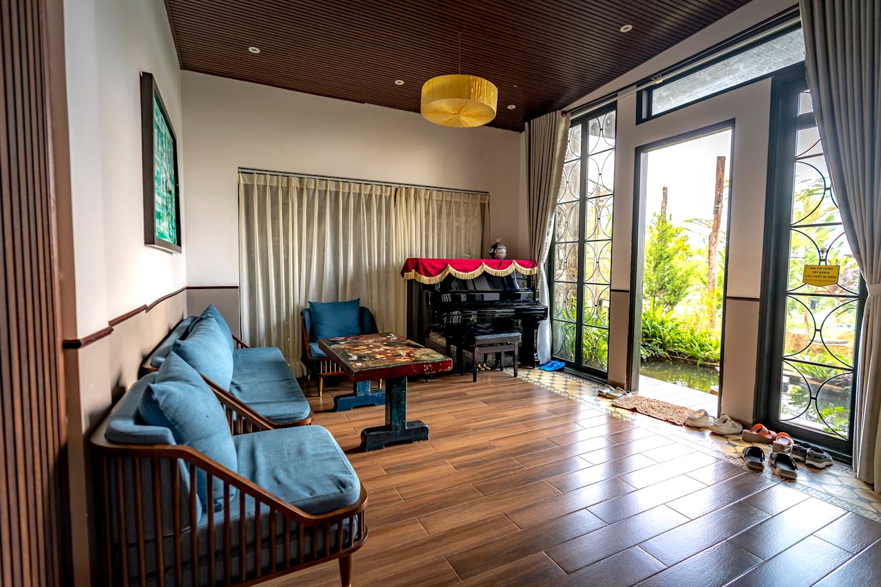 A stylish living room features a piano, chairs, and abundant natural light from large windows.