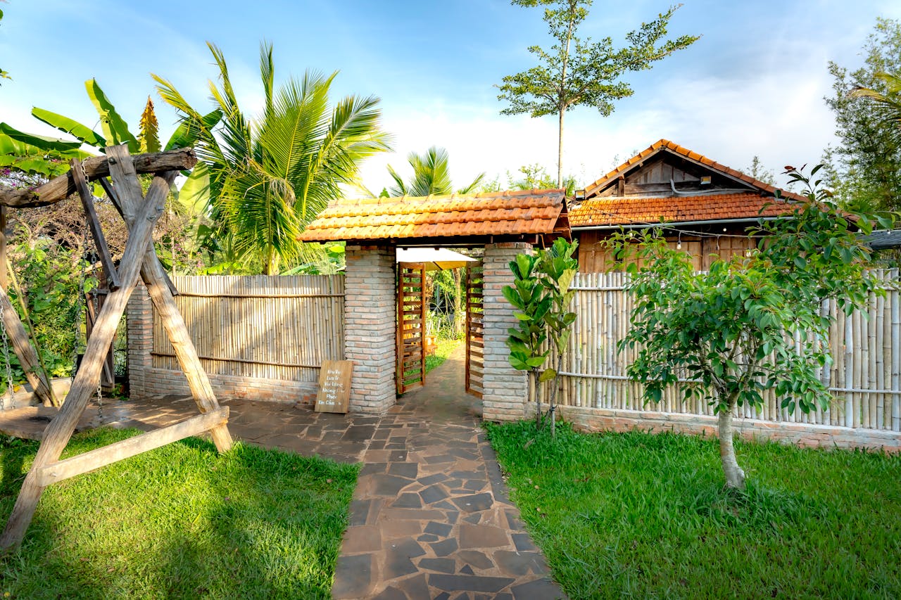 Inviting garden entrance featuring a wooden swing and lush greenery under a clear blue sky.